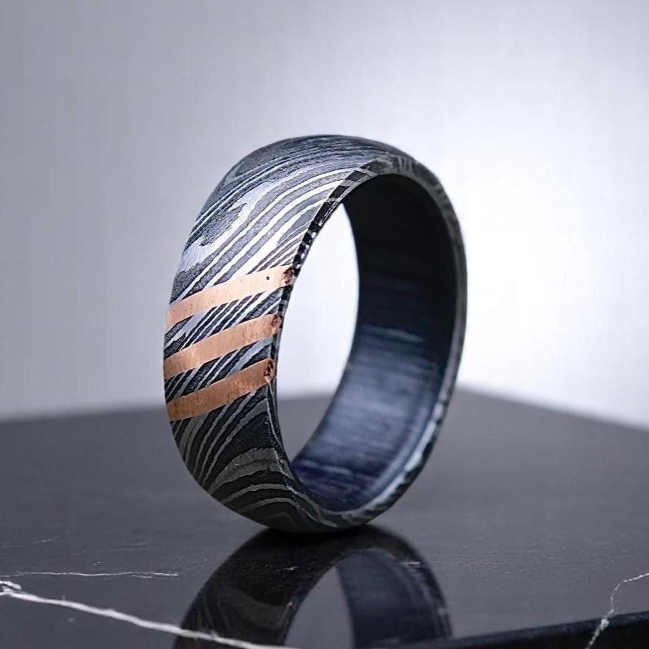 Woven patterned ring with metallic accents on a reflective surface