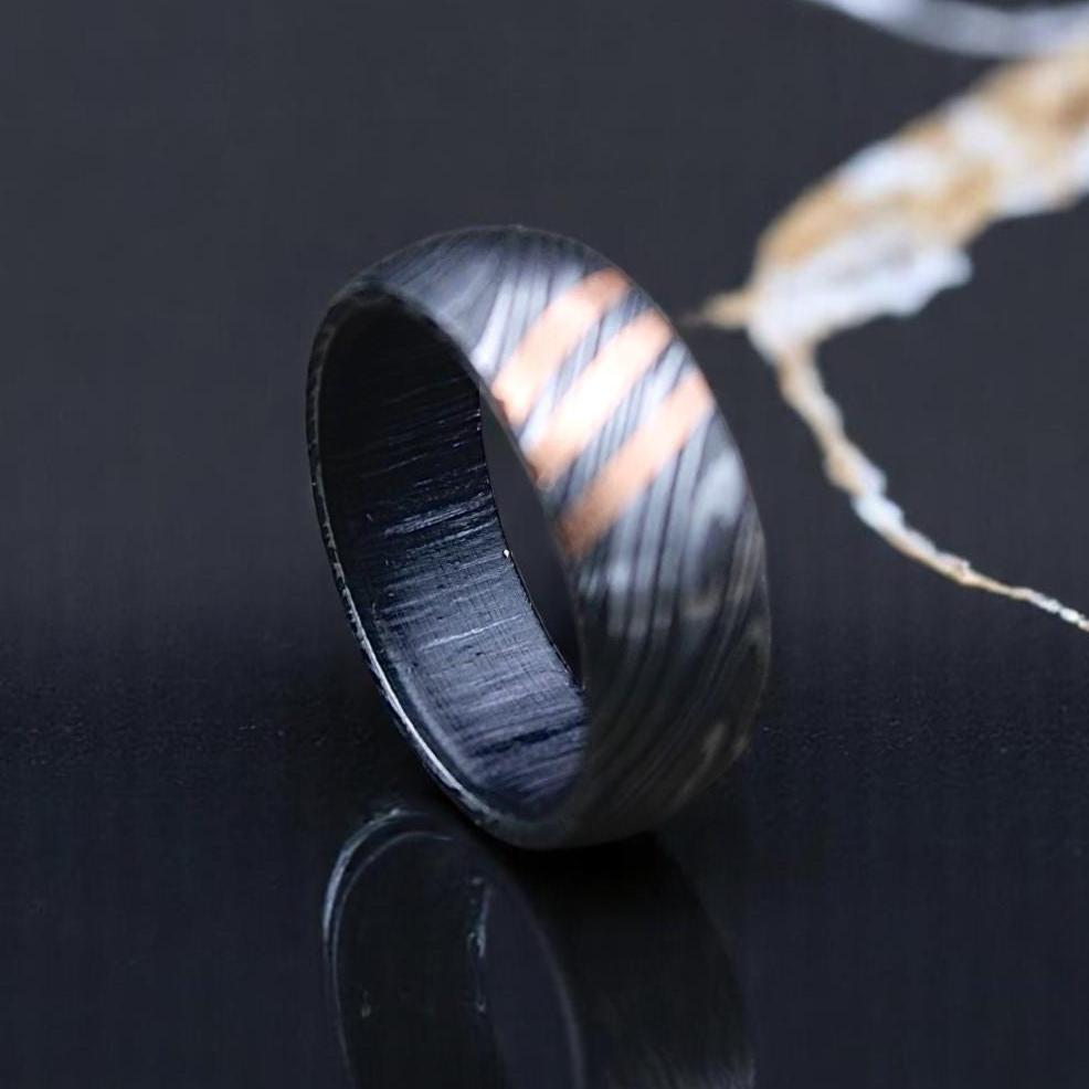 Black Damascus steel ring on a dark surface with a marble pattern