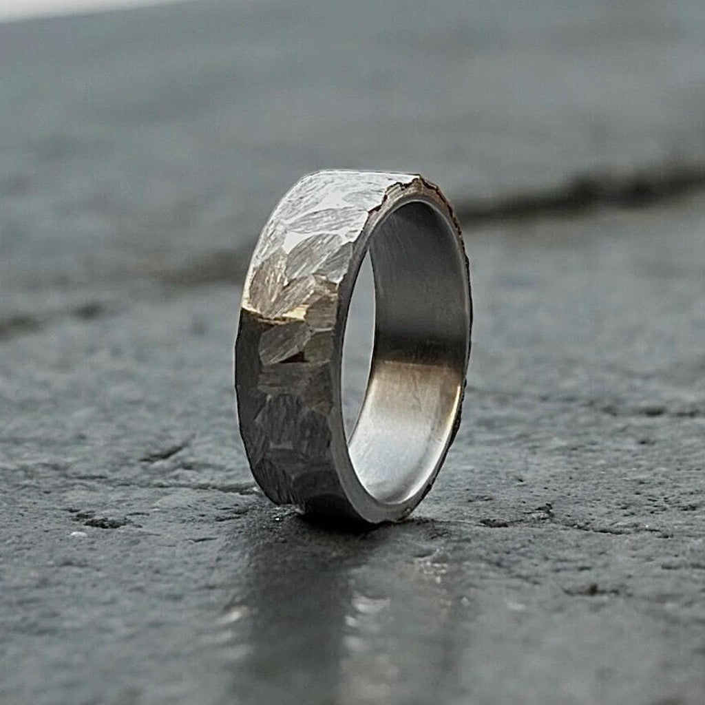 Silver ring with textured surface on a dark stone surface